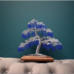 May include: A wire sculpture of a tree with blue beads representing blossoms. The tree is on a wooden base and is sitting on a light grey sofa.