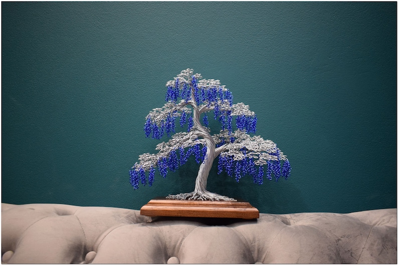 May include: A wire sculpture of a tree with blue beads representing blossoms. The tree is on a wooden base and is sitting on a light grey sofa.