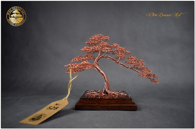 May include: A copper wire bonsai tree sculpture with a brown wooden base. The tree has a twisted trunk and branches with small copper wire leaves. The sculpture is labeled with the number "528".