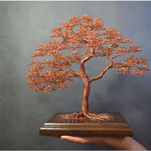 May include: A copper wire sculpture of a tree with a brown wooden base. The tree has a twisted trunk and branches with small copper leaves.