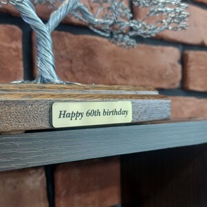 May include: A silver wire tree sculpture on a wooden base with a gold plaque that reads "Happy 60th birthday".