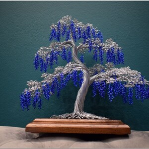 May include: A wire sculpture of a tree with blue and silver wire. The tree is on a wooden base.
