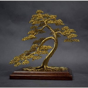 Op de afbeelding: Een gouden draadbeeld van een bonsaiboom op een houten voet. De boom heeft een dikke stam en veel takken met kleine, ronde bladeren.