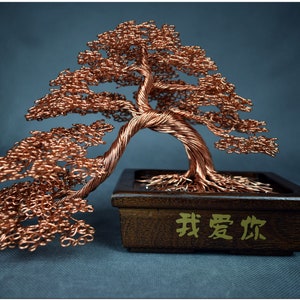 May include: A copper wire bonsai tree sculpture with a twisted trunk and branches. The tree is in a dark brown wooden pot with the Chinese characters "我爱你" (I love you) inscribed on the front.