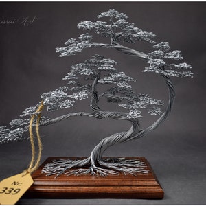 K&ouml;nnte beinhalten: Handgefertigte Bonsai-Baumskulptur aus Draht. Der Baum hat ein detailliertes Design mit silberfarbenem Draht, einschlie&szlig;lich Stamm, &Auml;sten und Bl&auml;ttern. Er ist auf einem rechteckigen Holzsockel montiert. Die Skulptur hat ein Etikett mit der Nummer 339.