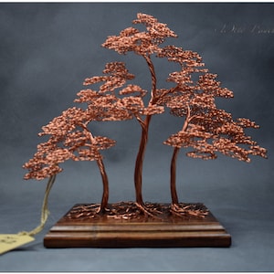 May include: A copper wire sculpture of three trees on a wooden base. The trees are arranged in a cluster, with the tallest tree in the center. The sculpture is a unique and decorative piece of art.
