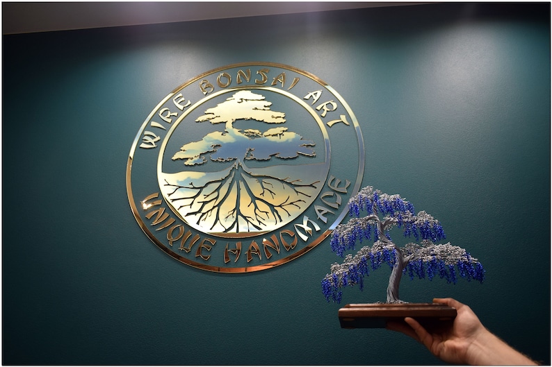 May include: A gold metal sign with the text "Wire Bonsai Art Unique Handmade" in a circle with a stylised tree and roots inside. A small blue and silver beaded bonsai tree is held in a hand.