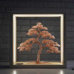 May include: A copper wire bonsai tree sculpture displayed in a wooden frame with a warm, glowing light. The tree has detailed branches and leaves, set against a dark brick wall. A small plant and clock are on the table.