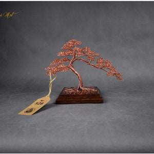 May include: A copper wire bonsai tree sculpture on a wooden base. The tree is styled with a cascading branch and has a tag with the number "528" on it. The sculpture is labeled "Wire Bonsai Art" and "Unique Handcrafted".