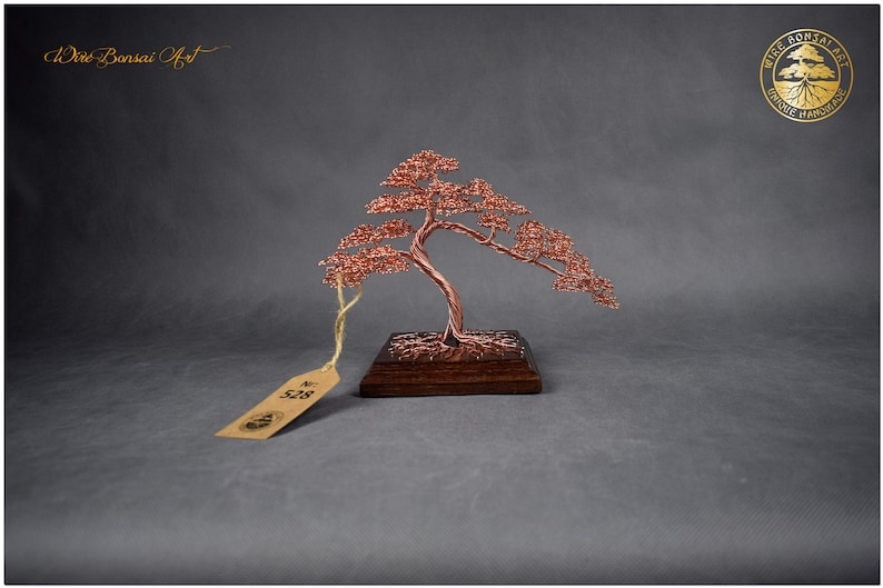 May include: A copper wire bonsai tree sculpture on a wooden base. The tree is styled with a cascading branch and has a tag with the number "528" on it. The sculpture is labeled "Wire Bonsai Art" and "Unique Handcrafted".