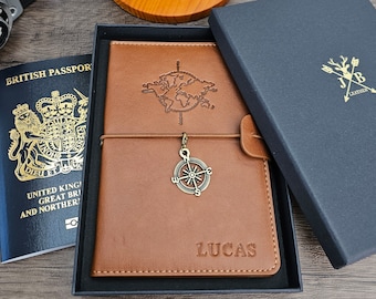 May include: A brown leather passport holder with a compass charm and the name "Lucas" embossed on the front. The holder is in a dark blue box with a leather logo.