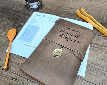 Peut inclure: Un journal relié en cuir marron avec le texte "Our Family Original Recipes" et un symbole de cœur. Le journal a un charme en métal avec un design de cuillère, de fourchette et de couteau.