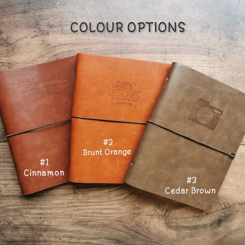 May include: Three leather journals in cinnamon, burnt orange, and cedar brown, each with a black elastic closure. The journals have embossed text and designs, including "Memories," "Create Memories," and a camera icon. The text "Colour Options" is at the top.