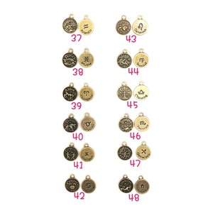 May include: A collection of antique gold-colored zodiac charms. Each charm features a zodiac symbol and a corresponding word, such as "Friendly" for Aquarius and "Intuitive" for Pisces. The charms are numbered from 37 to 48.