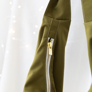 May include: A green fabric bag with a white zipper and white stitching. The bag has a fold-over top and a long strap.