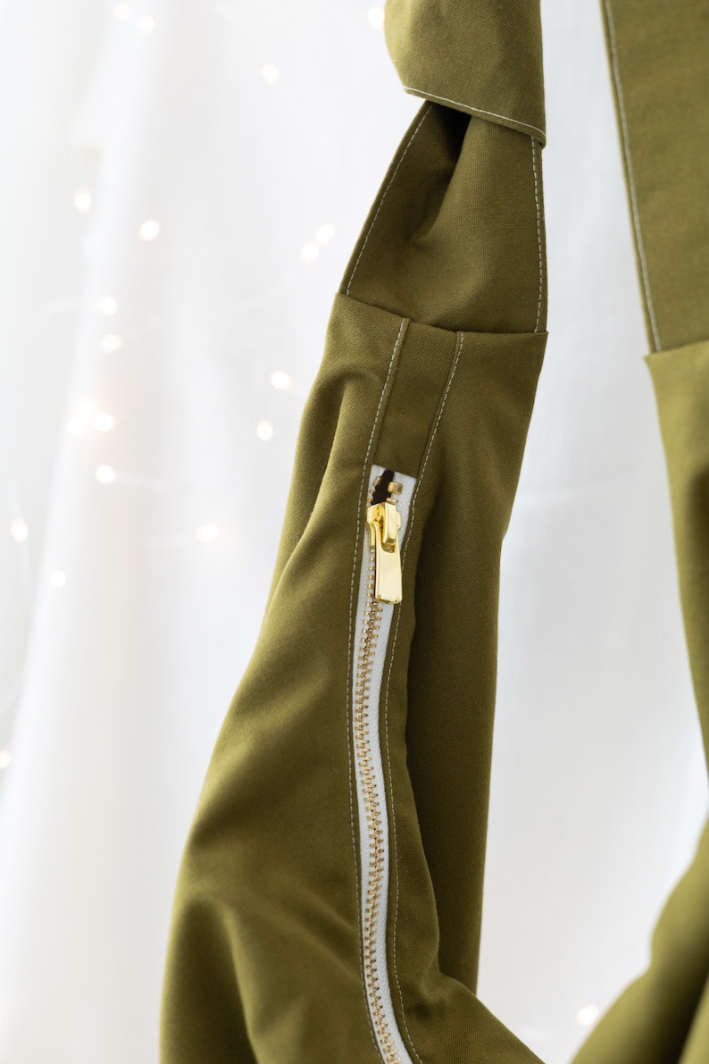 May include: A green fabric bag with a white zipper and white stitching. The bag has a fold-over top and a long strap.