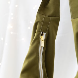Pode incluir: Uma bolsa de tecido verde com um z&iacute;per branco e costuras brancas. A bolsa tem uma parte superior dobr&aacute;vel e uma al&ccedil;a longa.