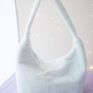 Pode incluir: Uma bolsa de ombro branca e fofa com uma &uacute;nica al&ccedil;a. A bolsa &eacute; feita de um material macio e felpudo.