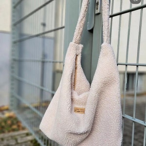 May include: A white fluffy tote bag with a zipper closure and a brown leather patch that says "A bag full of happiness".