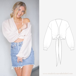 Könnte beinhalten: Ein weißes Crop-Top mit langen Ärmeln und einem Bindeverschluss vorne. Das Oberteil ist in der Taille gebunden und die Ärmel sind an den Handgelenken gerafft. Das Oberteil wird auf einem Model gezeigt, das eine Jeans-Shorts trägt.