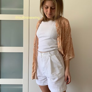 May include: White linen shorts with a button and zipper closure. The shorts have pleats in the front and are worn with a white t-shirt and a peach floral patterned shirt. The text '@butfirstsewing' is visible in the image.