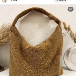 May include: A brown, fuzzy,  shoulder bag made of sherpa fabric. The bag has a single strap and a curved shape.