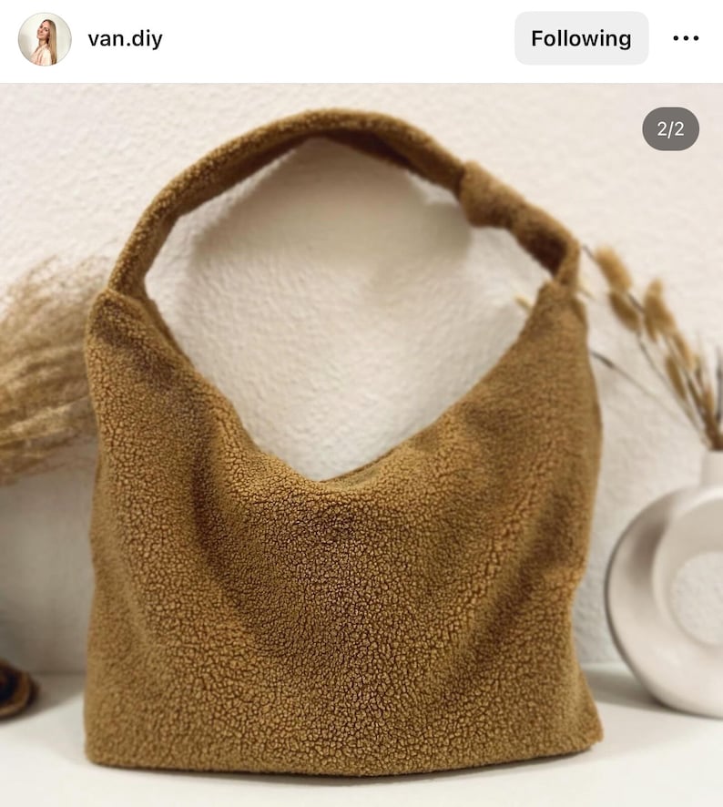 May include: A brown, fuzzy,  shoulder bag made of sherpa fabric. The bag has a single strap and a curved shape.