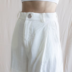 May include: White linen shorts with a button closure and pleats.
