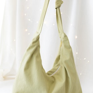 May include: A light green canvas tote bag with a single strap and a zipper closure.