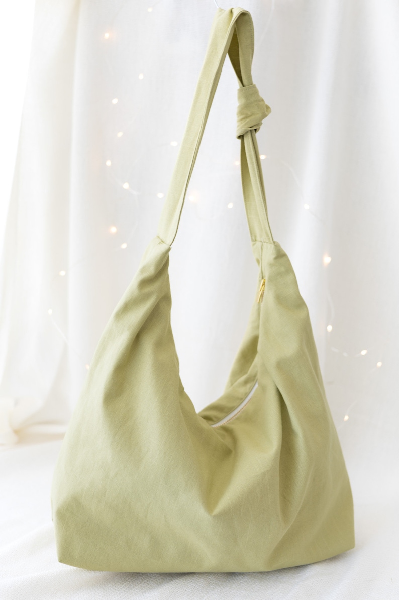 May include: A light green canvas tote bag with a single strap and a zipper closure.