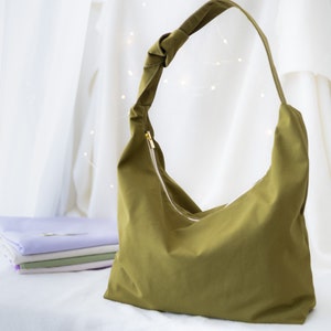 Pode incluir: Uma bolsa tote de tecido verde com uma al&ccedil;a de n&oacute; e um fecho de correr. A bolsa &eacute; feita de um material macio e dur&aacute;vel e tem um interior espa&ccedil;oso.