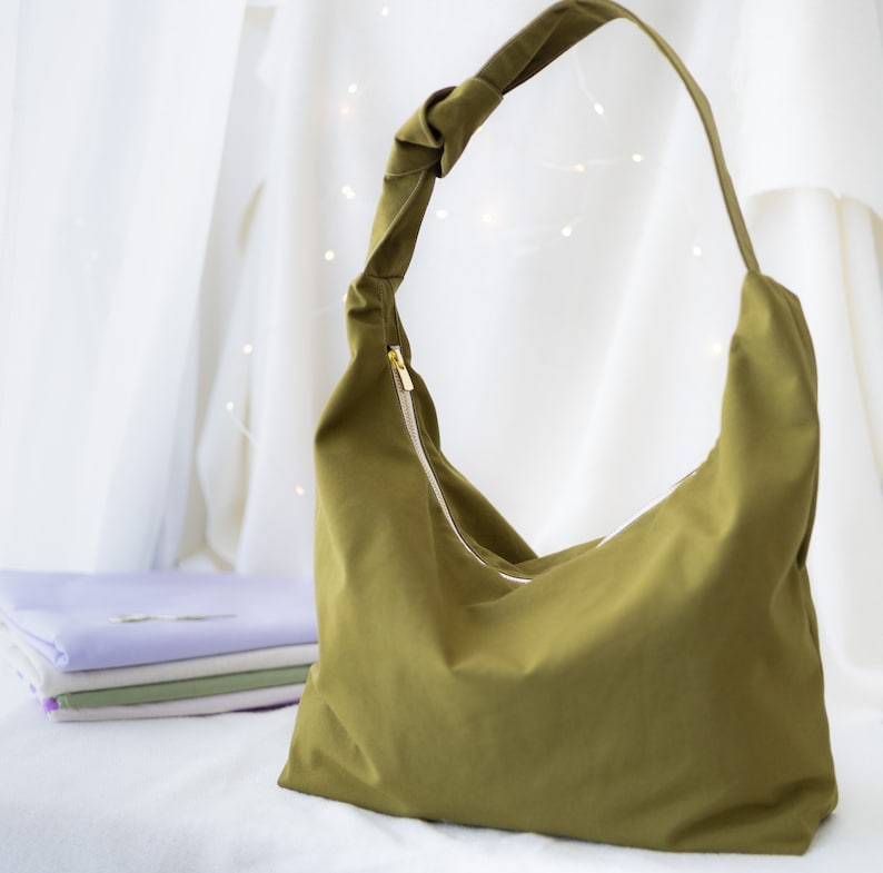 Pode incluir: Uma bolsa tote de tecido verde com uma al&ccedil;a de n&oacute; e um fecho de correr. A bolsa &eacute; feita de um material macio e dur&aacute;vel e tem um interior espa&ccedil;oso.