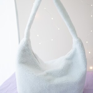 May include: A white fluffy shoulder bag with a single strap. The bag is made of a soft, fuzzy material.