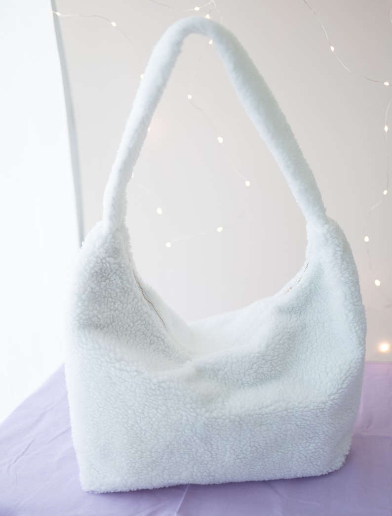 May include: A white fluffy shoulder bag with a single strap. The bag is made of a soft, fuzzy material.