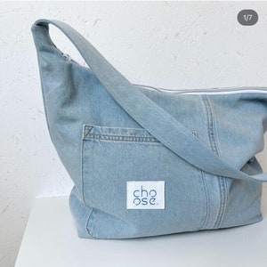 May include: A light blue denim tote bag with a white zipper and a white patch that says "choose." The bag has a long strap and a pocket on the front.