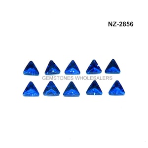 Puede incluir: Diez piedras preciosas triangulares azules, cada una con una superficie facetada, dispuestas en dos filas de cinco. Las piedras preciosas están sobre un fondo blanco. NZ-2856