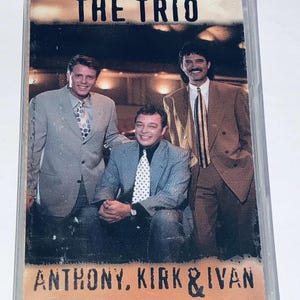 May include: A cassette tape with a picture of three men in suits. The text on the tape reads "THE TRIO ANTHONY, KIRK & IVAN".
