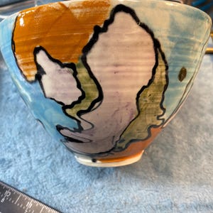 May include: A ceramic bowl with a blue, orange, green, and purple abstract design. The bowl is hand-painted and has a glossy finish.