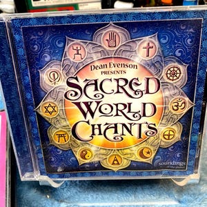 May include: A CD case with a blue background and a gold sunburst design. The text "Dean Evenson Presents Sacred World Chants" is in a stylized font. The case features various symbols, including a cross, a star of David, and a yin-yang symbol.