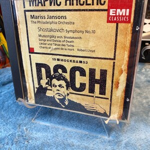 May include: A CD case featuring the album "Shostakovich Symphony No.10" by Mariss Jansons and The Philadelphia Orchestra. The cover has a vintage aesthetic with text and a portrait of a man. The EMI Classics logo is visible.