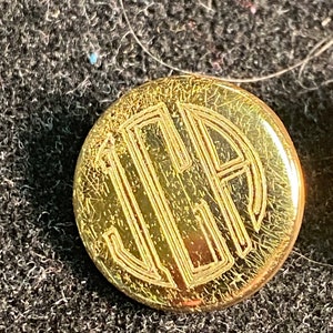 May include: A gold-colored button with a monogram of the letters "J.L.H." engraved in a circle.