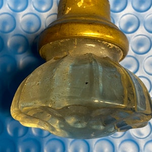 May include: A clear glass door knob with a gold metal base. The knob has a faceted design and is slightly worn.