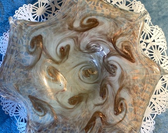 May include: A white glass bowl with a starburst shape and a swirling pattern of brown and gold. The bowl is sitting on a white doily.
