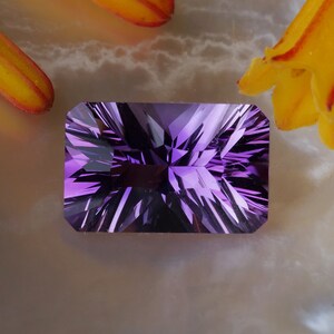 May include: A deep purple amethyst gemstone with a rectangular cut and a starburst pattern. The gemstone is faceted and has a high polish.