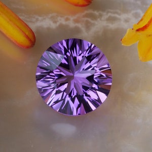 Puede incluir: Una gema de amatista redonda y facetada con un patrón de estrella. La gema es de color púrpura intenso y está rodeada de pétalos de flores amarillas y naranjas.