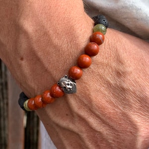 May include: A beaded bracelet with red, green and black beads. A silver lion head charm is attached to the bracelet.
