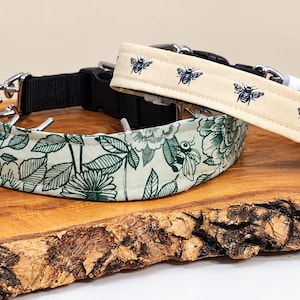 May include: Two pet collars with black plastic buckles and metal hardware. One collar features a cream fabric with a repeating dark blue bee pattern, while the other displays a light green fabric with a dark green floral and leaf print design.