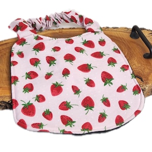 Può includere: Una bavaglino per neonati rosa chiaro con un motivo ripetuto di fragole rosse con foglie verdi e piccoli puntini bianchi. Il bavaglino presenta un bordo inferiore arrotondato e un'apertura del collo elasticizzata per una facile vestibilità.