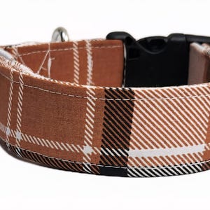 May include: A brown and white plaid dog collar with a black plastic buckle and silver-colored metal hardware. The collar is made of fabric and features a classic plaid pattern. The collar is designed for pets.