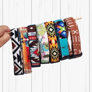 Puede incluir: Una colección de collares para perros estampados, cada uno con un diseño único. Los collares muestran una variedad de colores y patrones, incluyendo formas geométricas, motivos del suroeste e impresiones florales. Se sujetan con una clavija de madera.